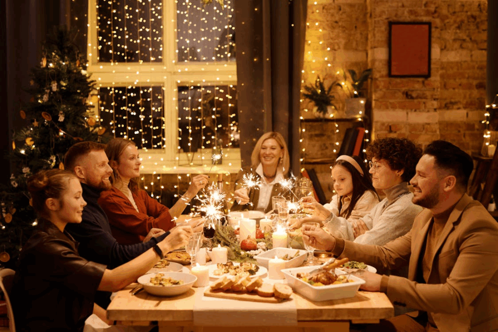 A joyful family gathers around a festive Christmas dinner table, holding sparklers and sharing a meal, with warm string lights and a decorated tree in the background.