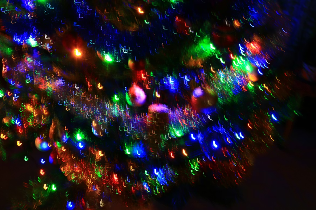 A festive Christmas tree decorated with traditional multicolor lights in blue, green, red, and orange, creating a vibrant and colorful holiday display with a glowing, slightly blurred effect.