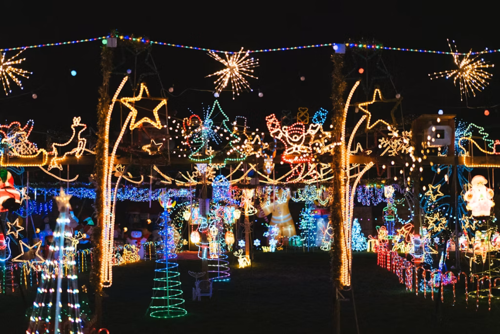 A vibrant and colorful Christmas lights display featuring illuminated stars, Santa figures, reindeer, trees, and festive decorations covering an outdoor yard at night.